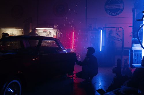 Free A mechanic repairs a car in a neon-lit garage, creating a unique and vibrant atmosphere. Stock Photo