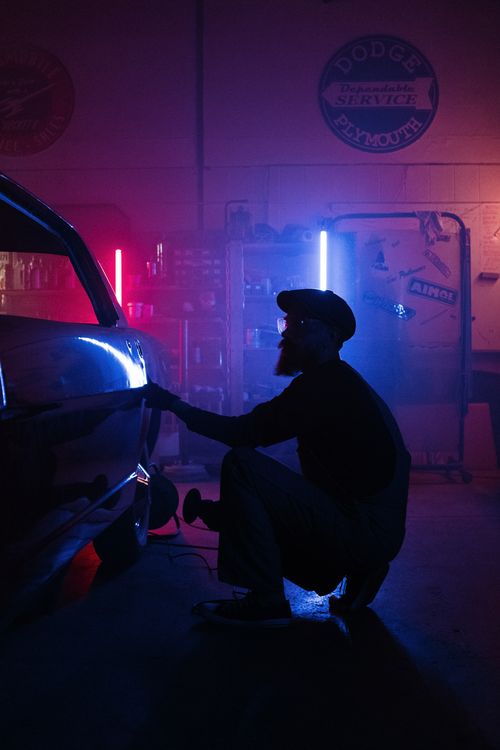 Free Silhouette of mechanic repairing a car in a dimly lit garage with colorful neon lights. Stock Photo