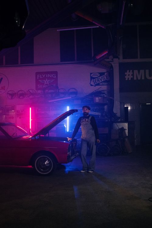 Free Mechanic working on a vintage car under neon lights in a dim garage setting. Stock Photo