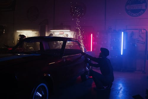 Man in Black Jacket and Black Pants Standing Beside Black Car during Nighttime