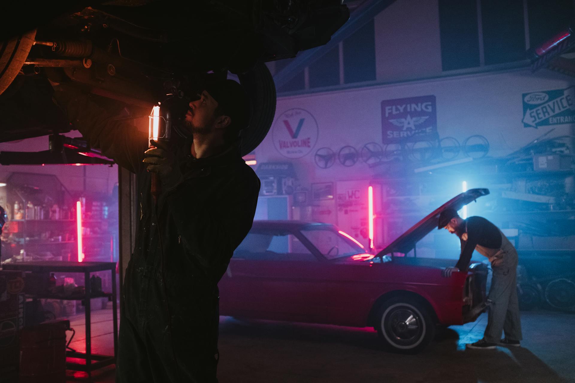 Mechanics working on vehicle in neon-lit garage with stylish retro car.