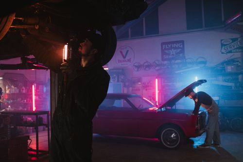 Free Mechanics working on vehicle in neon-lit garage with stylish retro car. Stock Photo