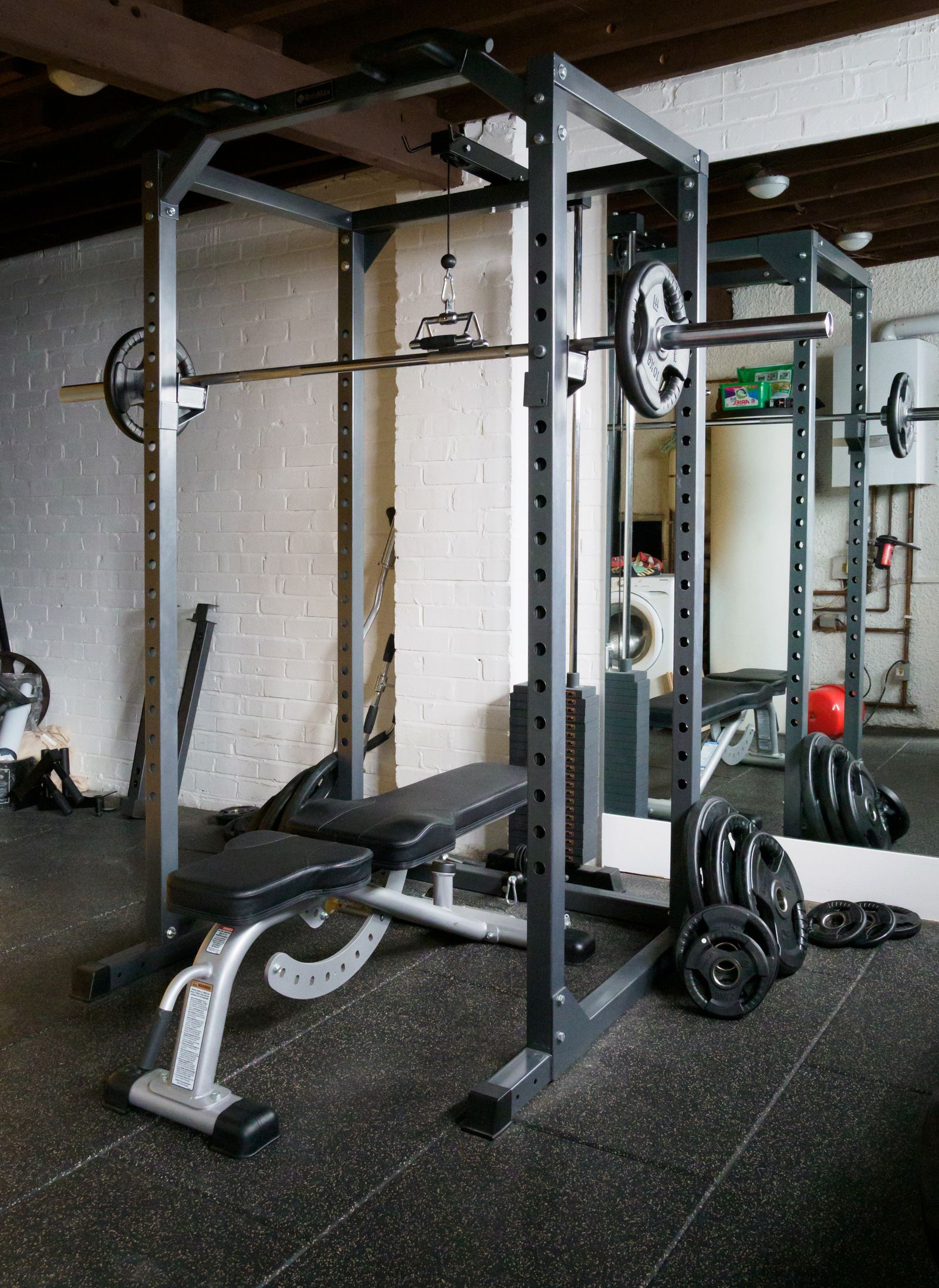 A home gym power rack setup with a barbell, weight bench, and wall mirror