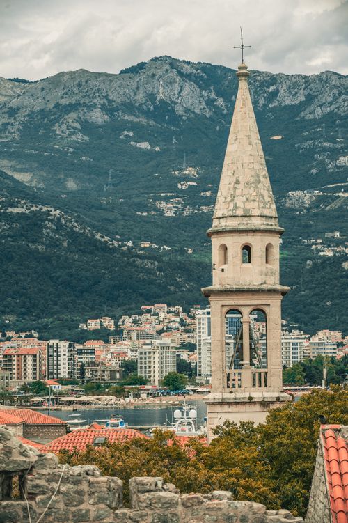 Free Aged stone church with cross on top near contemporary multistage houses and green mounts under cloudy sky in Montenegro Stock Photo