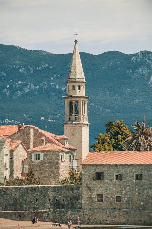 Free Ancient masonry church with cross on top near shabby building facades behind ridge in Montenegro Stock Photo