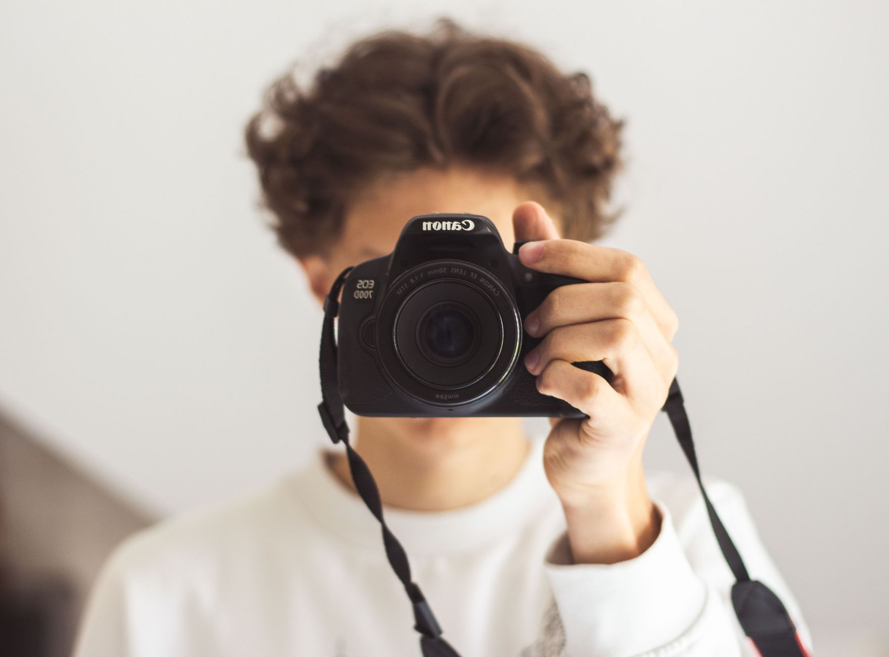 人像鏡頭等效焦段全解析:精準控制背景虛化 A young adult holding a Canon DSLR camera, capturing a portrait close-up.