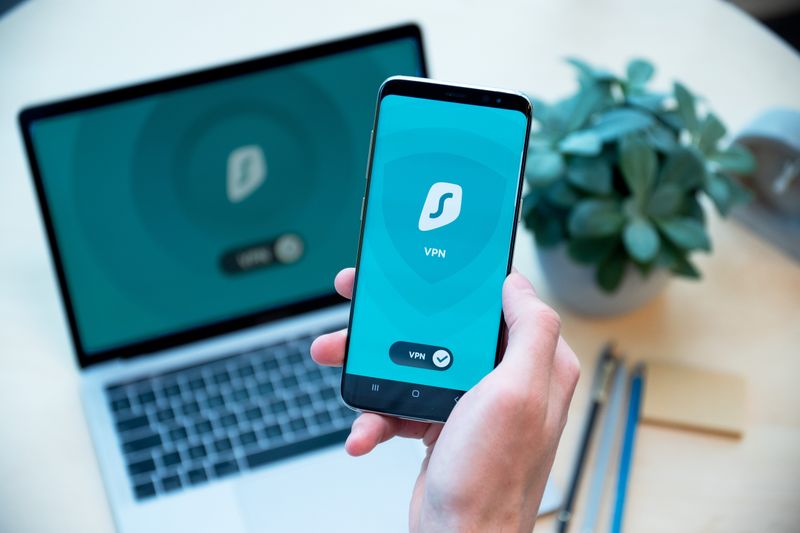 Close-up of a hand holding a smartphone with VPN app, laptop in the background, showcasing digital security.