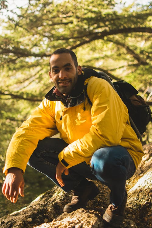 Man in Yellow Jacket Carrying a Backpack Sitting on a Tree Log
