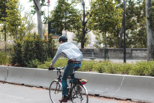 Back view full length male in casual wear and helmet riding modern bicycle along asphalt roadway amidst lush greenery
