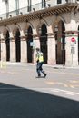 Side view full body traffic police officer in uniform and high visibility vest walking on asphalt road near arched building on sunny weather
