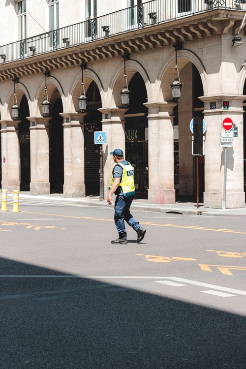 Free Side view full body traffic police officer in uniform and high visibility vest walking on asphalt road near arched building on sunny weather Stock Photo