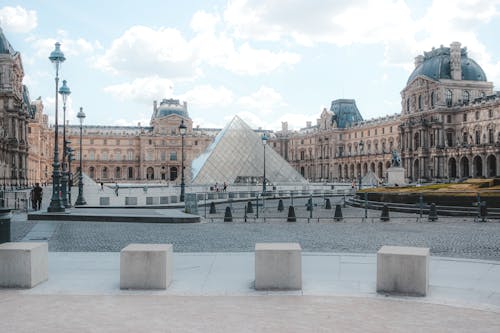 Exterior of historic Louvre Museum build in Gothic style near famous landmark glass Pyramid located in center of Paris on summer day