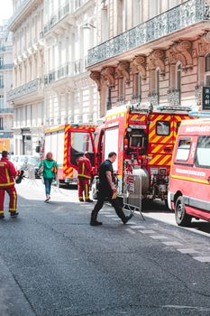 Firefighters in red uniforms walking on road near emergency service vehicles in historical city district
