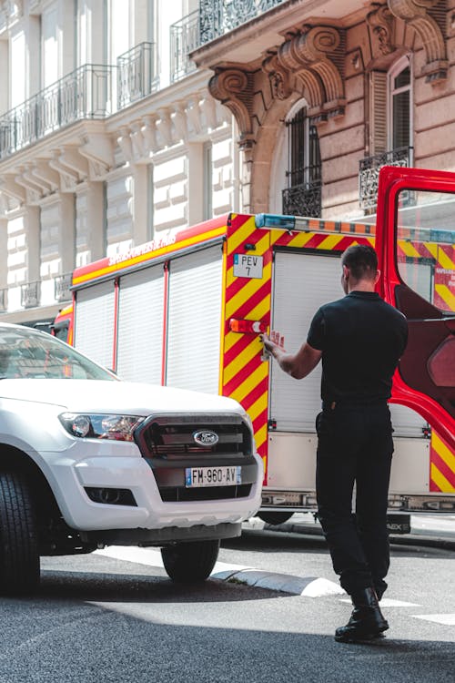 Back view of male in black uniform on carriageway with emergency vans showing driver on white crossover car place for parking