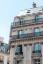 From below of old residential house with ornamental french windows and common balconies on upper floors and walls in form of colummns and roof chimney under blue sky
