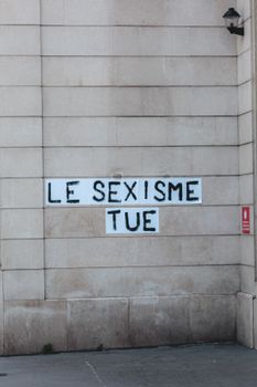 Inscription Le Sexisme Tue in French language written with black letters on white background on modern building wall