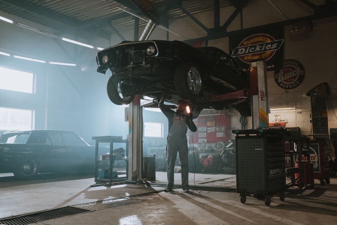 Mechanic inspecting a lifted classic car under work light