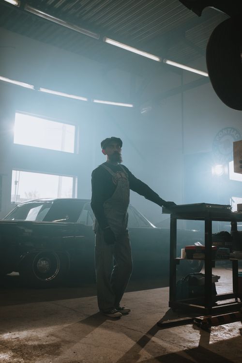 Free Bearded mechanic standing in a vintage car garage, ready for repair. Stock Photo