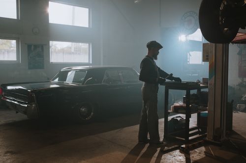 Free A mechanic working on a classic car in a dimly lit garage, showcasing vintage automotive repair. Stock Photo