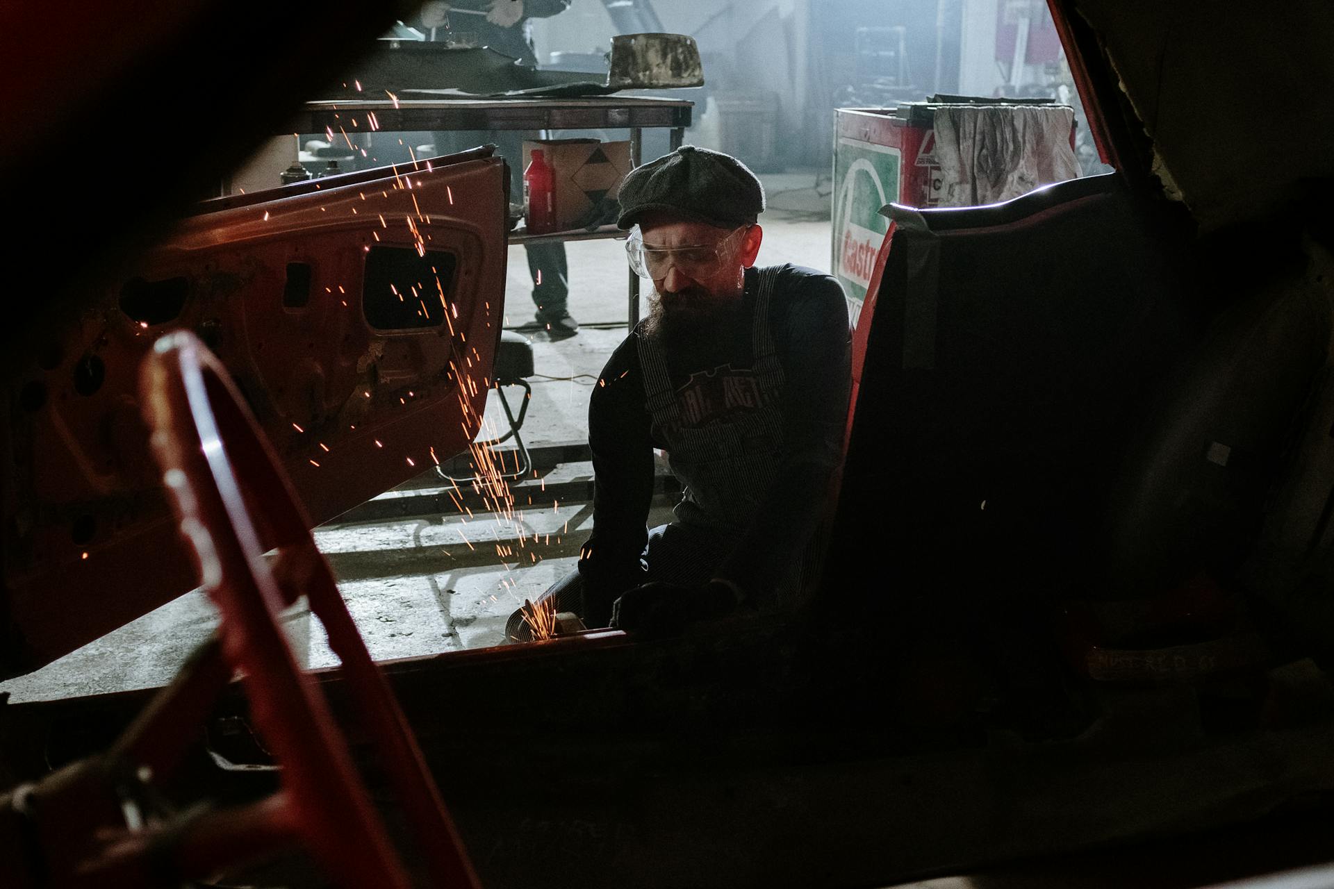 A mechanic welding inside an auto repair shop with flying sparks, focused on car restoration work.