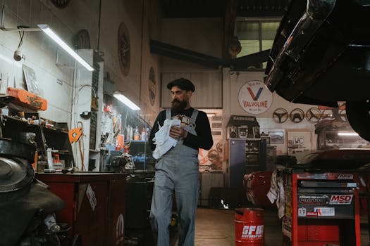 Mechanic in a classic garage setting, surrounded by tools and vehicles, working on a car repair.