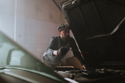 Man in Black Jacket and Black Pants Sitting on Green Car