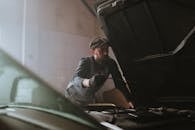 一名男性机械师在光线昏暗的车库里，正专注于检查汽车引擎盖下的情况