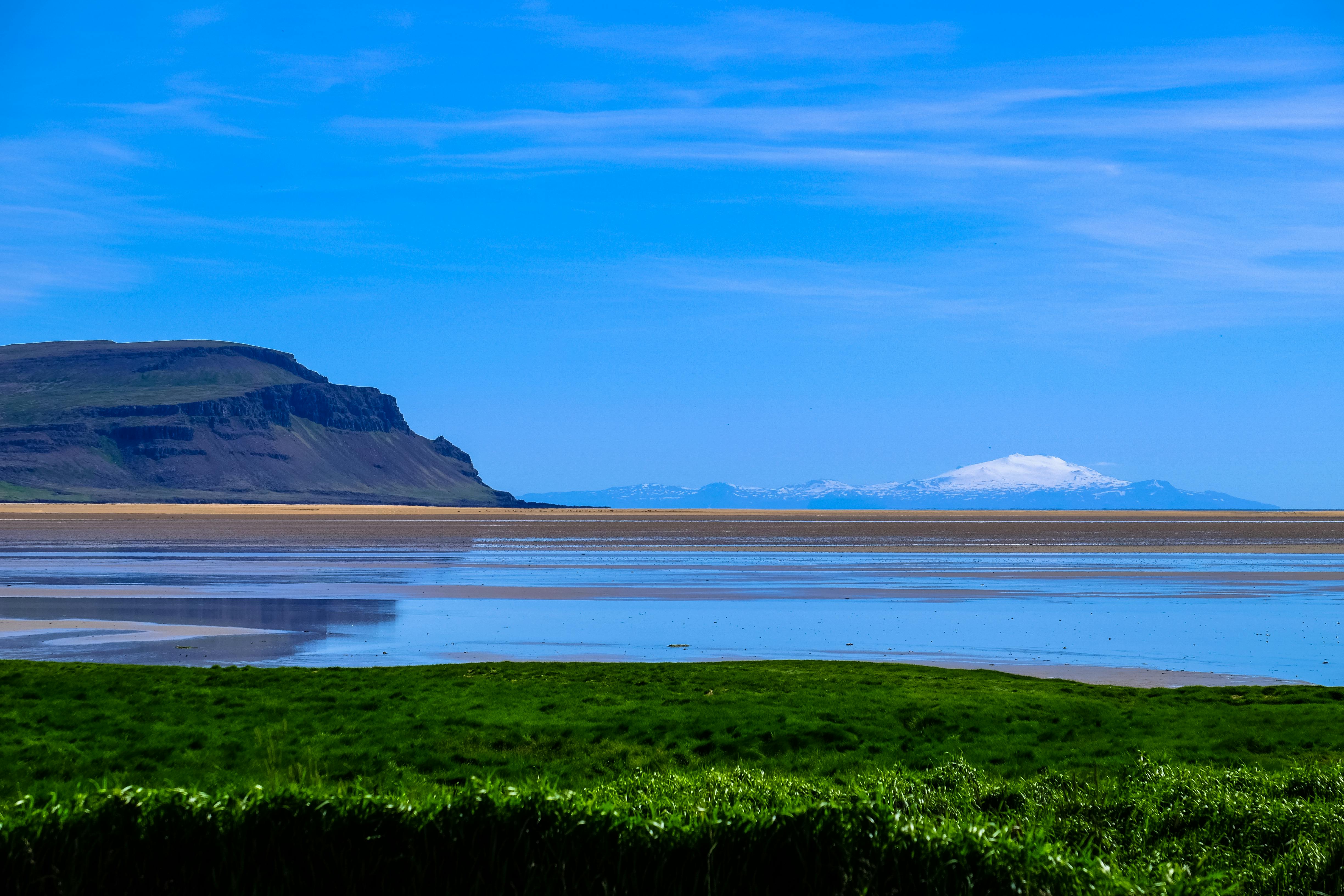 宁静的海岸景观中，悬崖、海洋和远处的雪山在蓝天下交相辉映