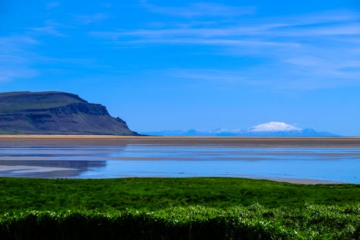 宁静的海岸景观中，悬崖、海洋和远处的雪山在蓝天下交相辉映