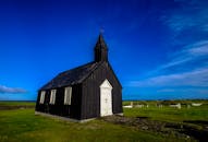 在风景如画的乡村中，一座古色古香的黑色木制教堂矗立在蔚蓝的天空下