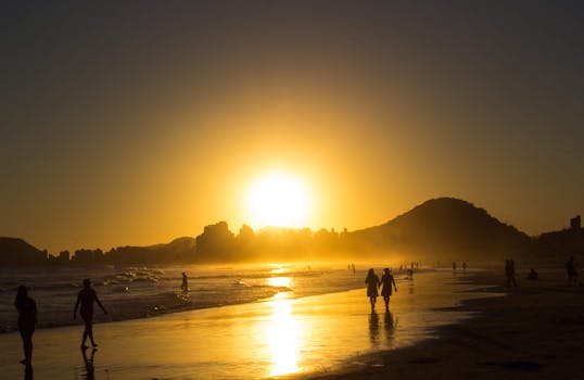 Silhouettes at sunset on Guarujá beach, Brazil, with a golden skyline.