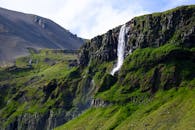 岩石山下，一道瀑布充满活力地倾泻而下，四周绿植葱郁，天空晴朗