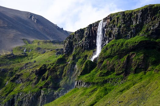 岩石山下，一道瀑布充满活力地倾泻而下，四周绿植葱郁，天空晴朗