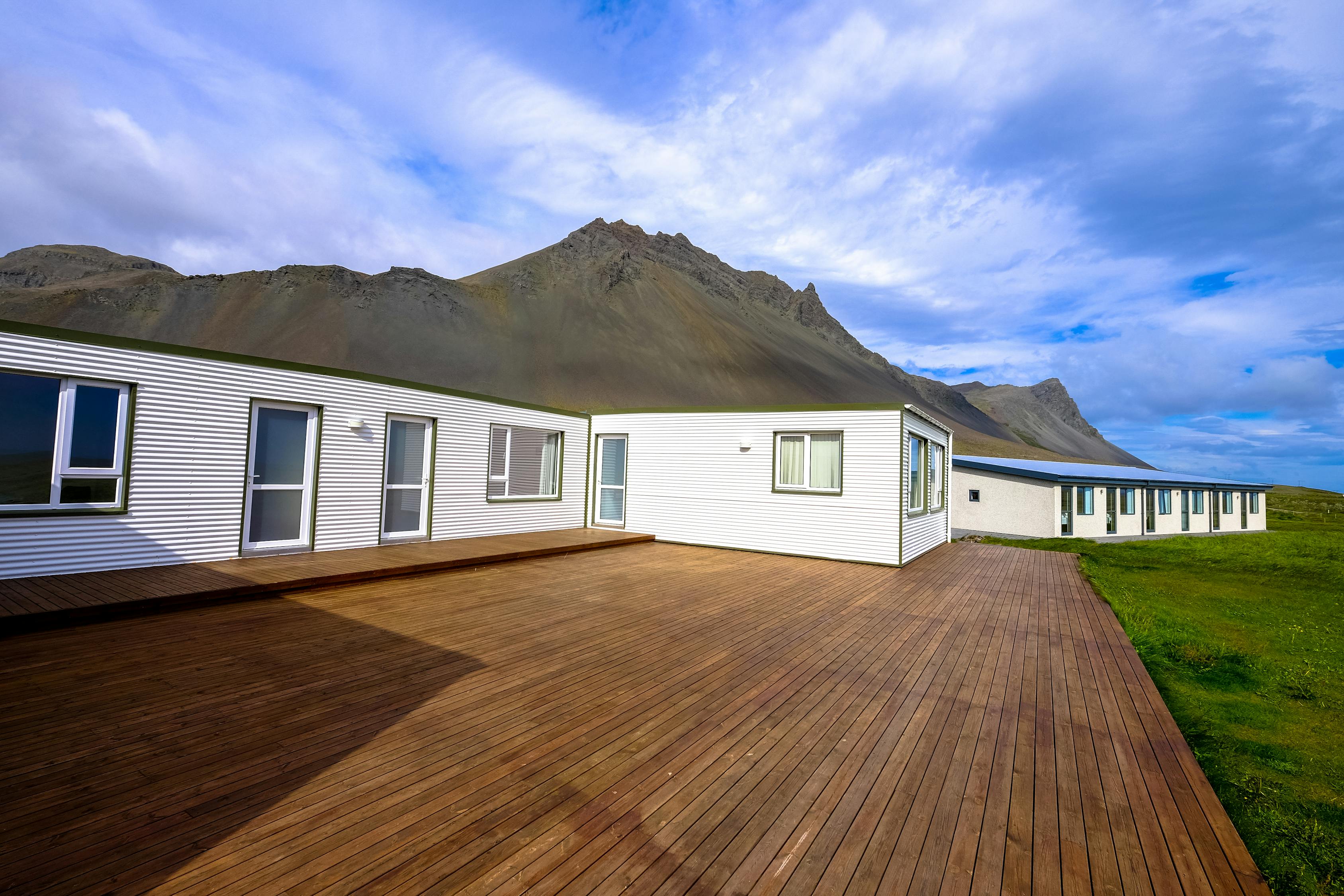 A white vinyl sided house attached to a beautifully restored wooden deck near a mountain and grass field