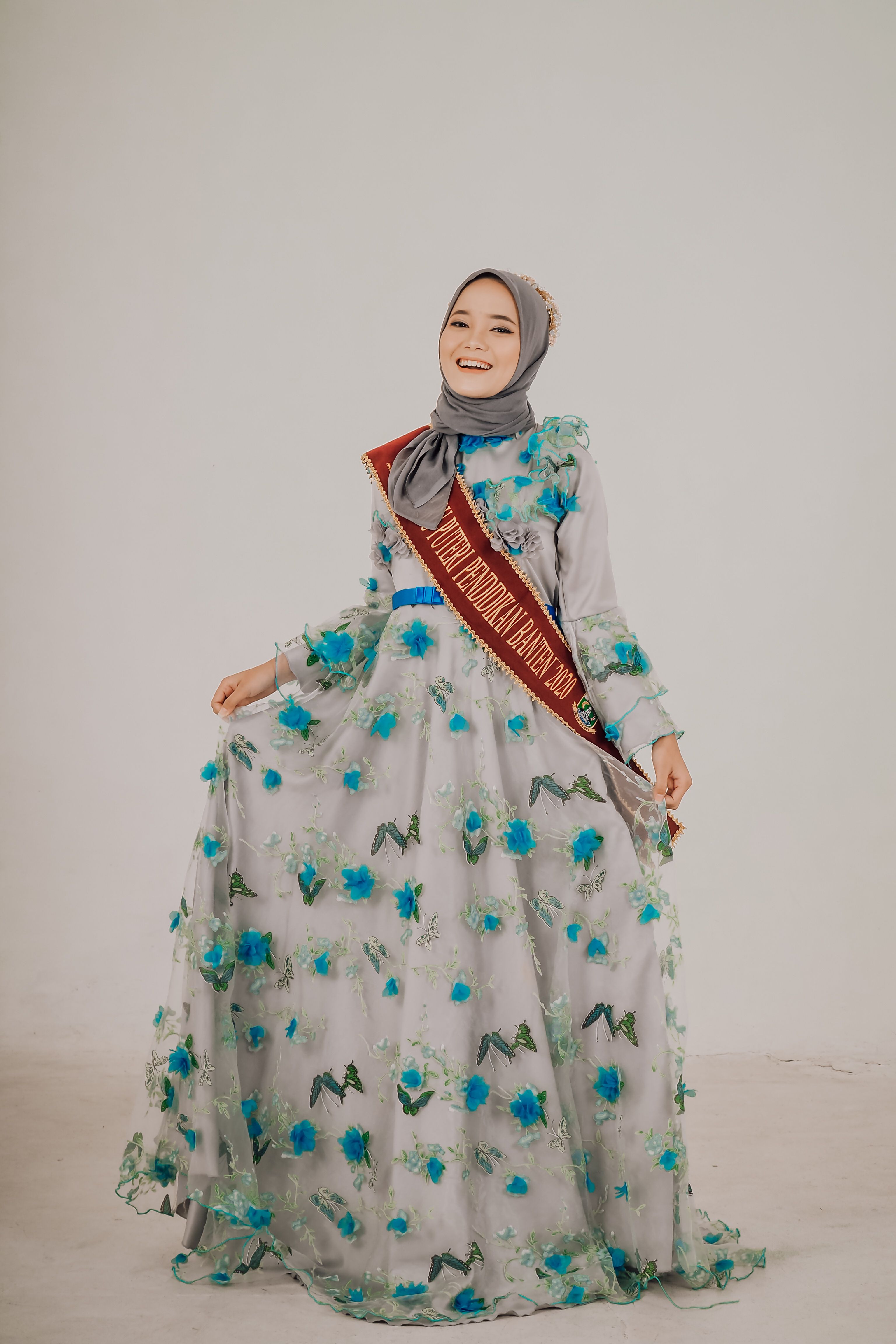 Stylish young woman in a floral hijab dress, proudly wearing a sash.