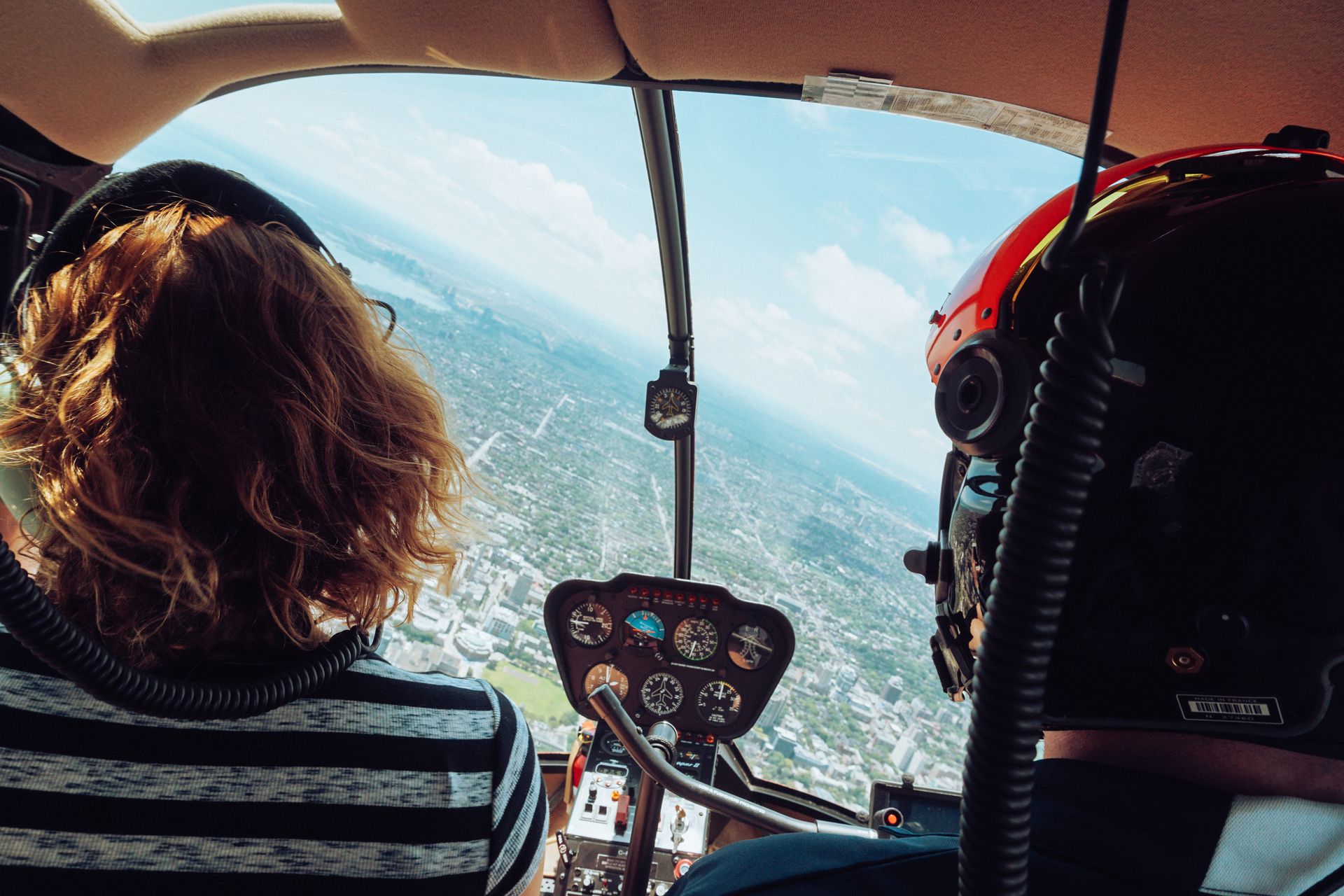 Back view of unrecognizable travelers in headsets admiring view of city during flight in helicopter