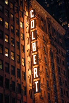 Vertical shot of the illuminated Colbert sign on a NYC building at night.