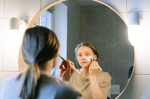 Mirror Reflection of a Woman Applying Facial Cream