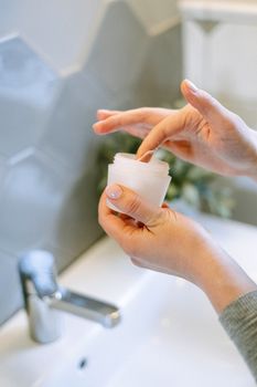 Close-up of hands applying cream in a modern bathroom, emphasizing skincare routine.