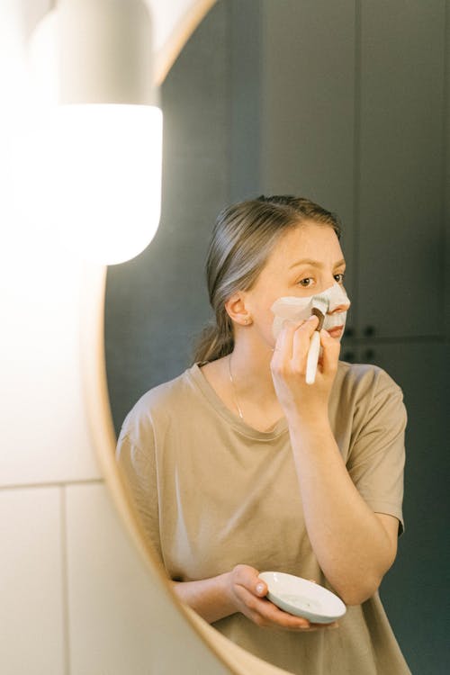 Mirror Reflection of a Woman Applying Face Cream