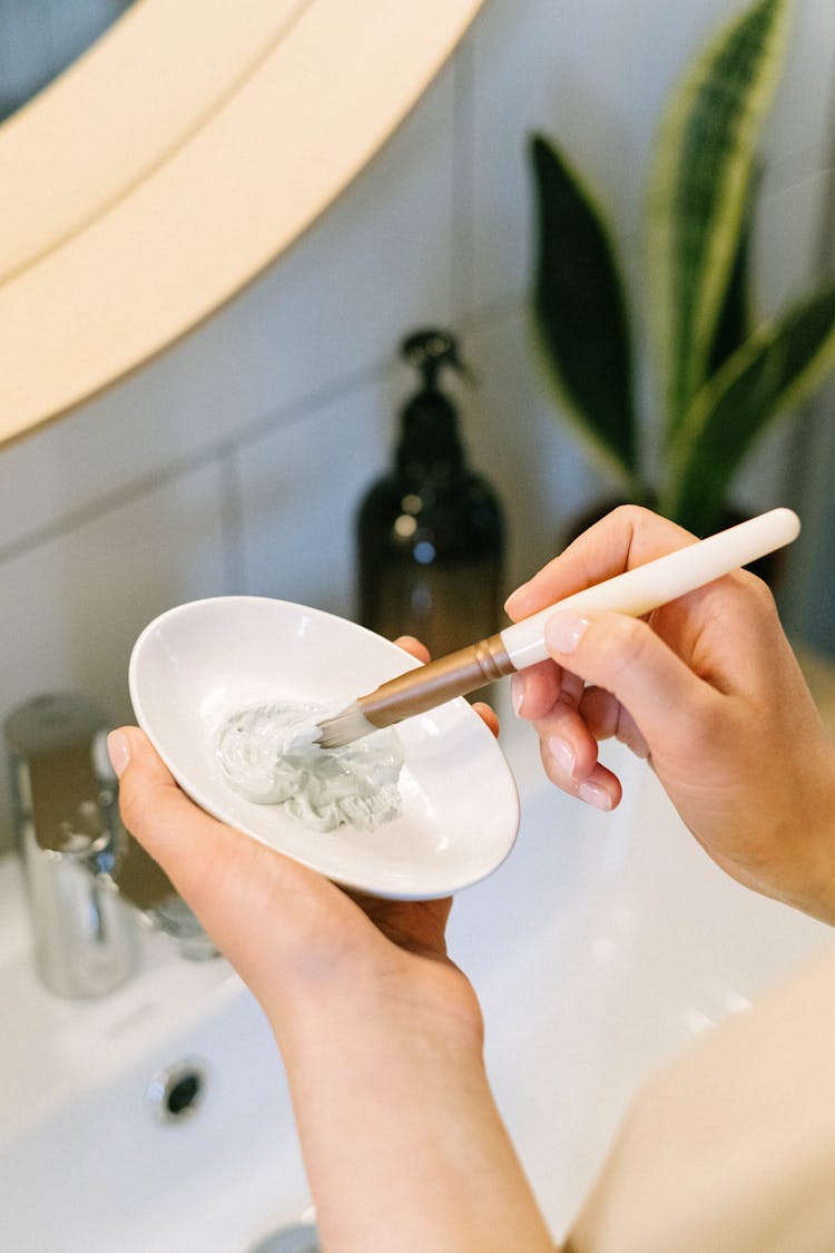 Hands Of A Person Holding A Saucer With Cream And A Makeup Brush