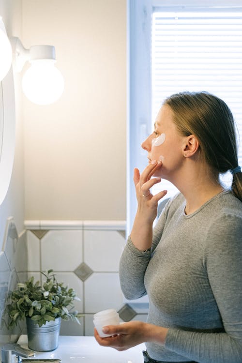 Woman in Gray Long Sleeve Shirt Applying Face Cream