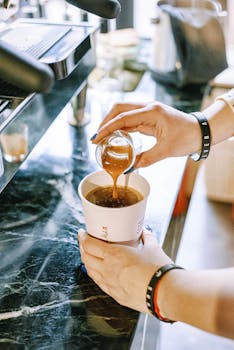 Close-up of a barista expertly pouring espresso into a paper cup on a marble countertop.