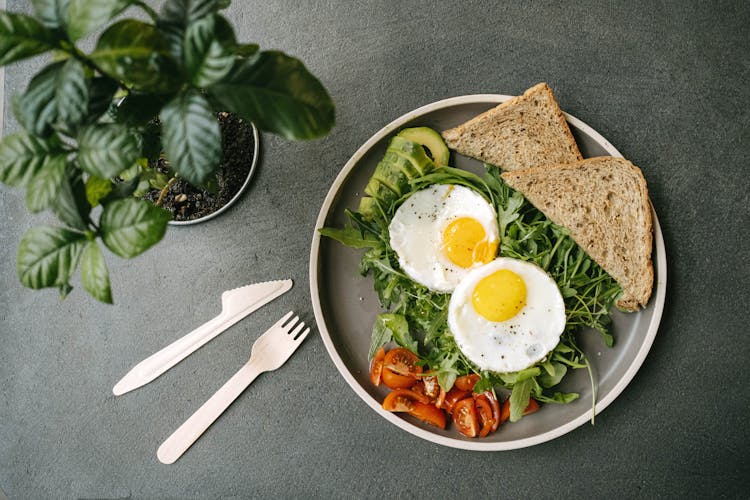 A Ceramic Plate With Eggs And Vegetables Near The Green Plant