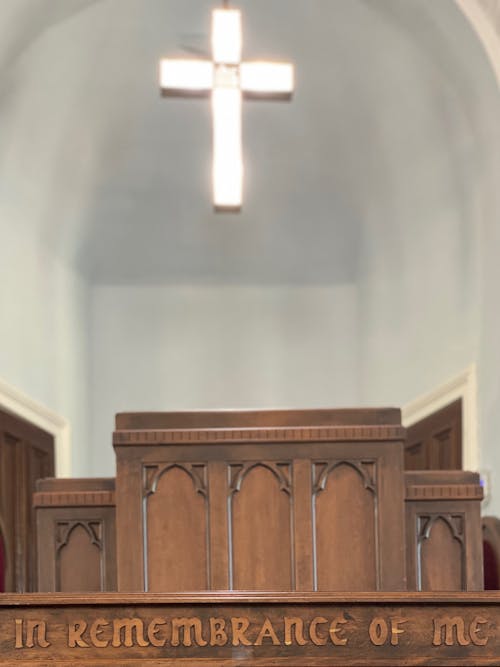 Illuminated cross hanging over aged carved wooden altar with In remembrance of me inscription in church