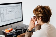 在轻办公室工作期间，一位无法识别的短发妇女侧身坐在计算机显示器前阅读文档，她戴着眼镜