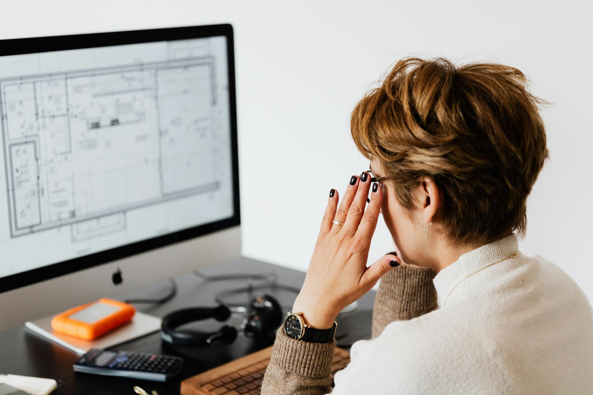 Side view of unrecognizable short haired woman wearing eyeglasses while reading documents on computer monitor during work in light office