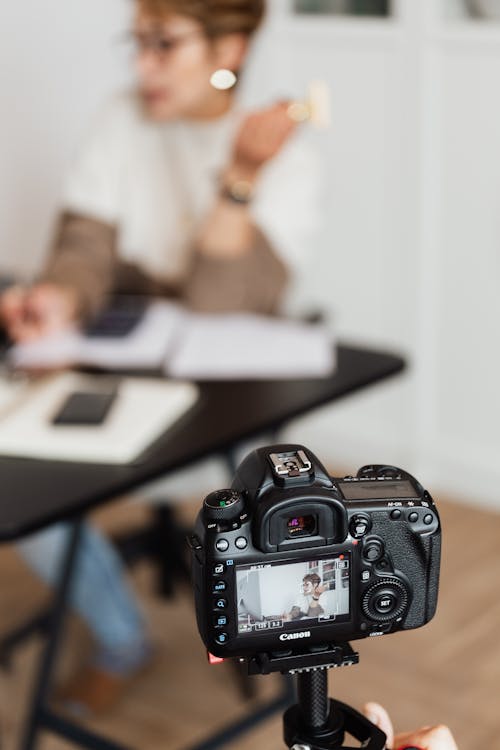 Anonymous person taking photo of busy unrecognizable woman on professional camera during work in modern studio