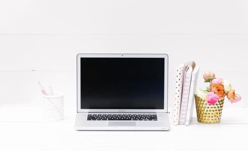 Free Minimalist workspace featuring a laptop, notebooks, and vibrant floral decor on a white surface. Stock Photo