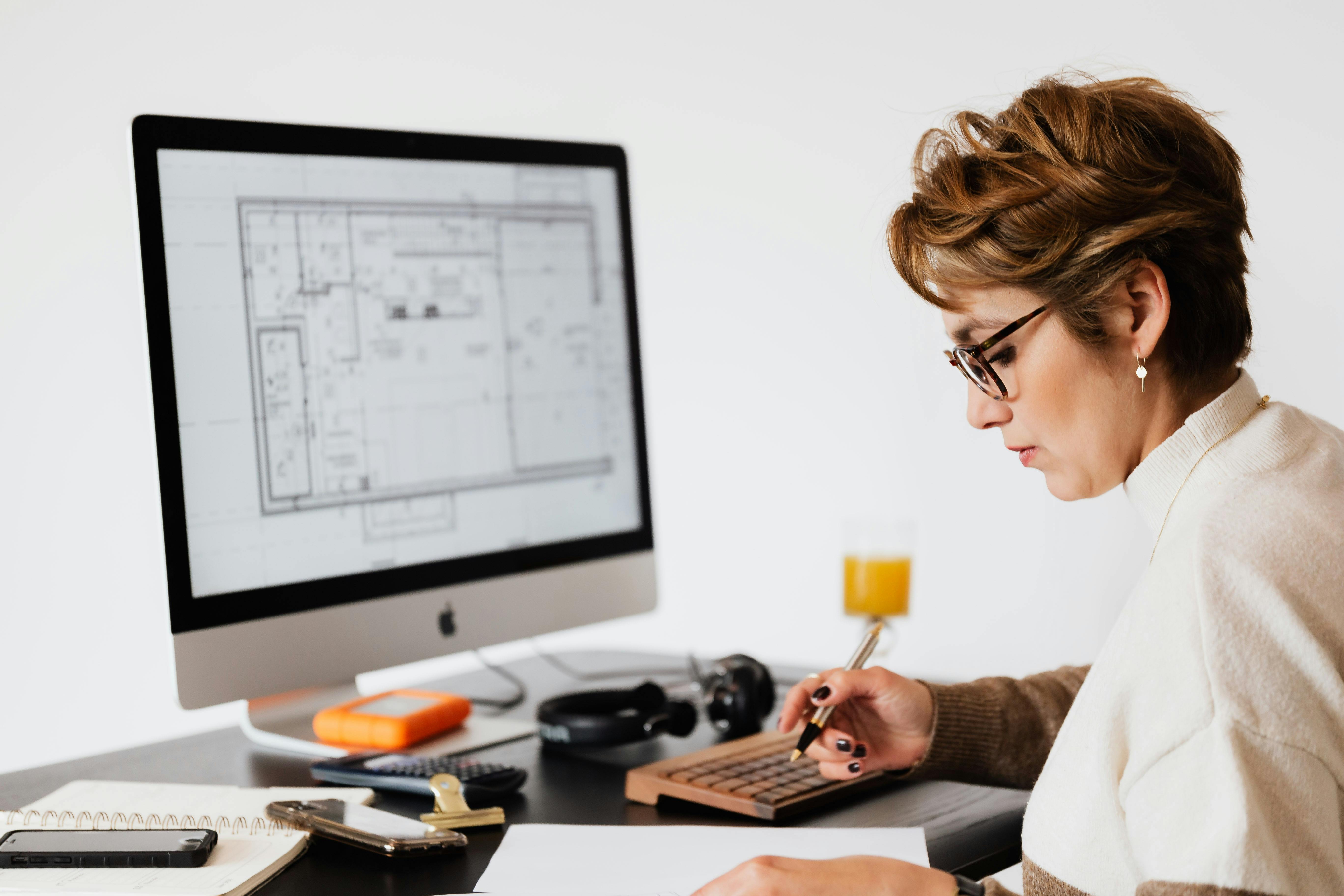 focused woman editing paper documents during work at desk with computer